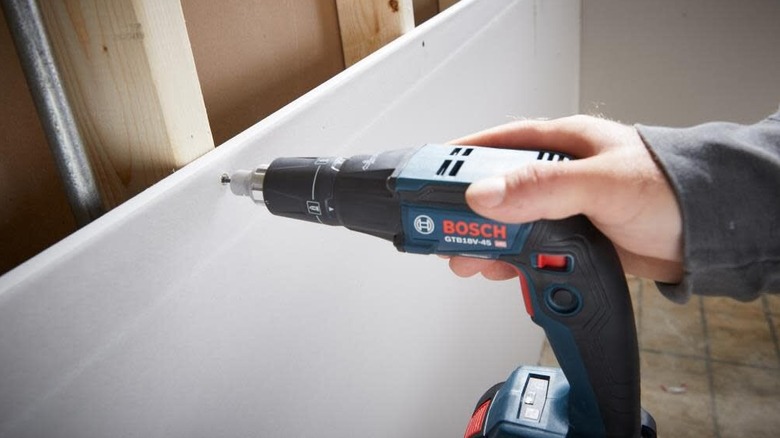 Applying a screw into a piece of drywall using the hex screwgun, using one hand.