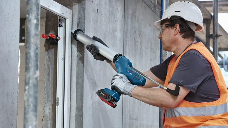 A construction worker using the caulk and adhesive gun on a window joint.