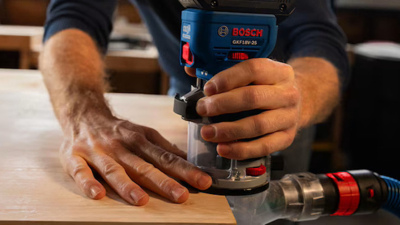 Bosch palm router being used on the side of a piece of lumber with the vacuum attachment