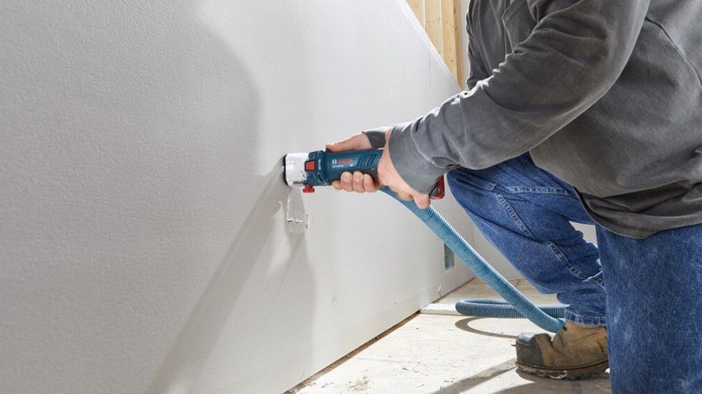 Bosch's 18V cut-out tool being used to slice a hole through drywall while attached to a vacuum