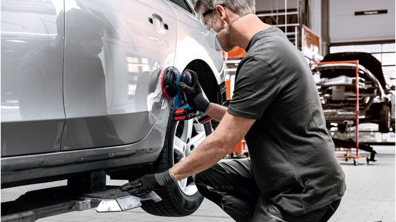 Work moves the random orbit sander along the side of a car to clean up the paint