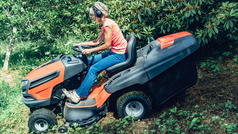 Woman using a lawn tractor down a slope.