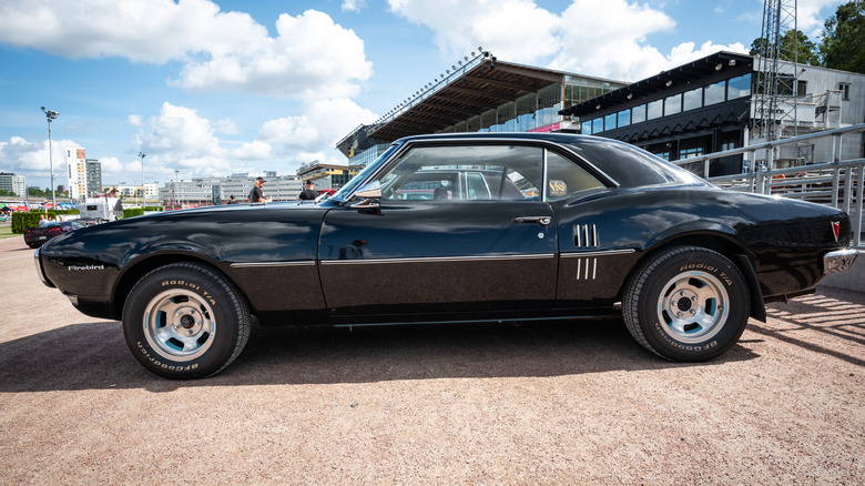 Side view of black 1967 Pontiac Firebird outside a race track
