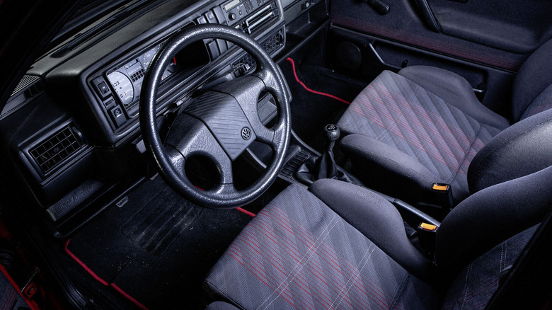 Interior view of a Mk2 Volkswagen GTI from the 1980s, featuring gray cloth sport seats with red plaid pattern.