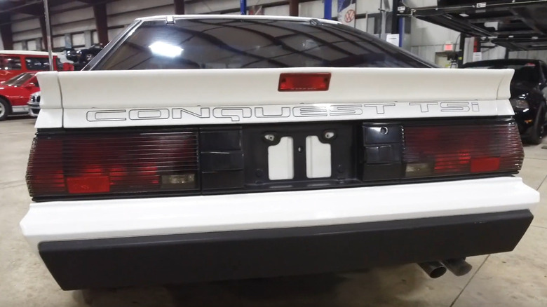 A rear view of a white 1987 Chrysler Conquest TSI sports coupe, showing its large silver "CONQUEST TSi" lettering across the hatch.