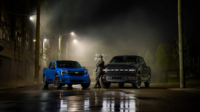 A man standing with two Ford trucks at night