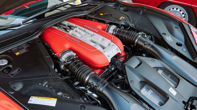 Ferrari F140 V12 engine on display under the open hood of a red Ferrari 812 Superfast