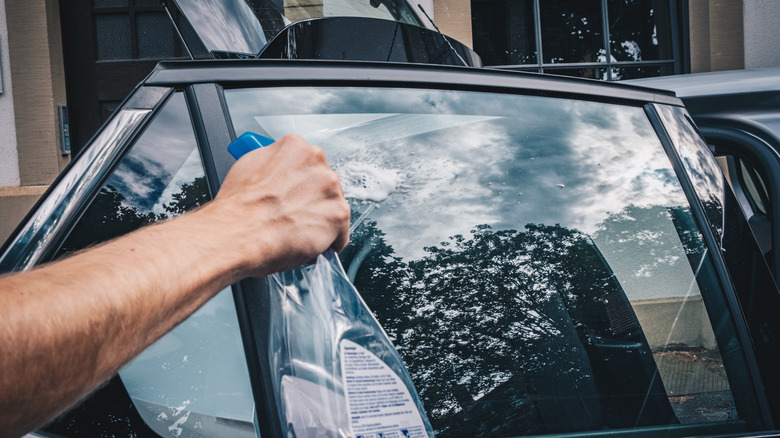 A person spraying a window cleaner on a car window