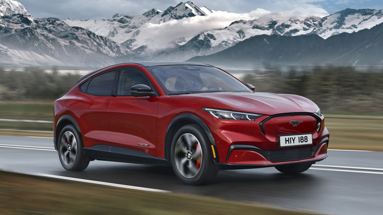 Red Ford Mustang Mach-E driving on a rural road with snowy mountains in the distance