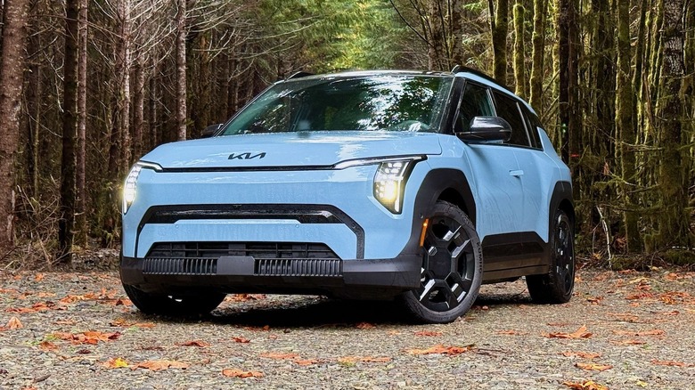 2027 Kia EV3 parked in a forest with tall trees and leaves on the ground