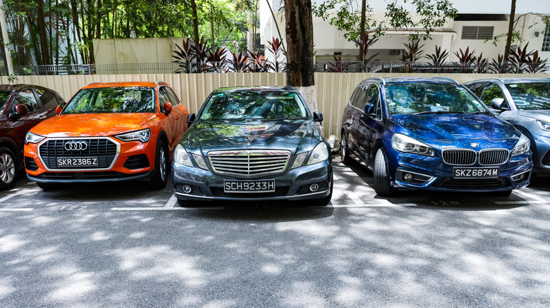 An Orange Audi crossover, black Mercedes sedan, and blue BMW hatchback parked together at the side of a road.