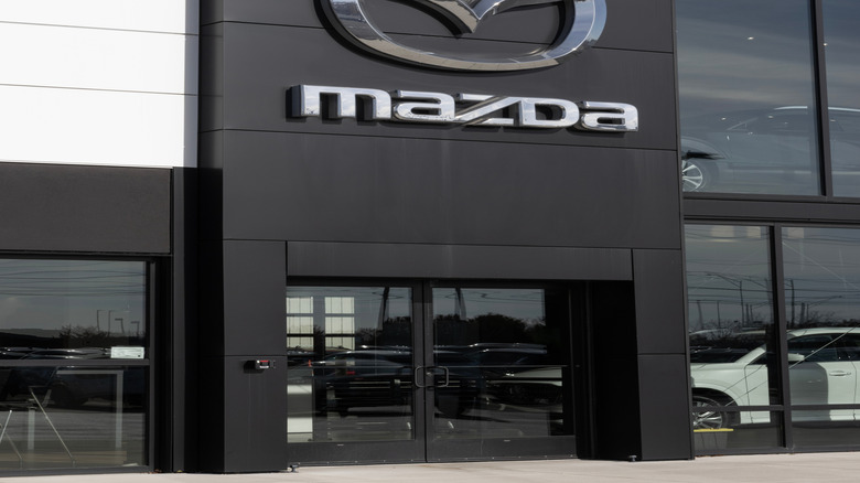 A silver Mazda logo mounted on a black feature wall outside a dealer.