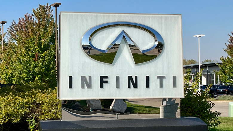 A silver Infiniti logo mounted onto a white concrete statue in a garden.