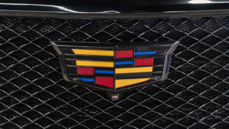 The iconic multicolored Cadillac shield mounted to the black grill of an unknown vehicle.