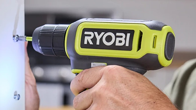 A person using a Ryobi drill on a cupboard.