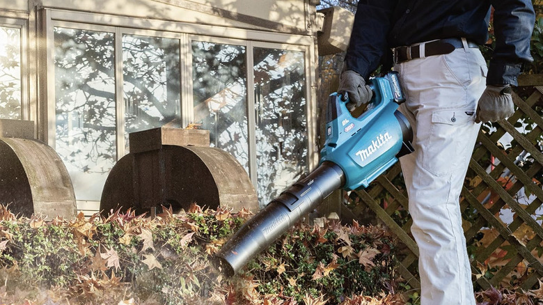A man wearing gloves using a Makita brushless blower to clear leaves