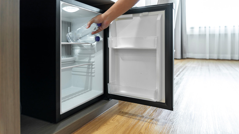Hand grabbing water bottle from mini fridge.