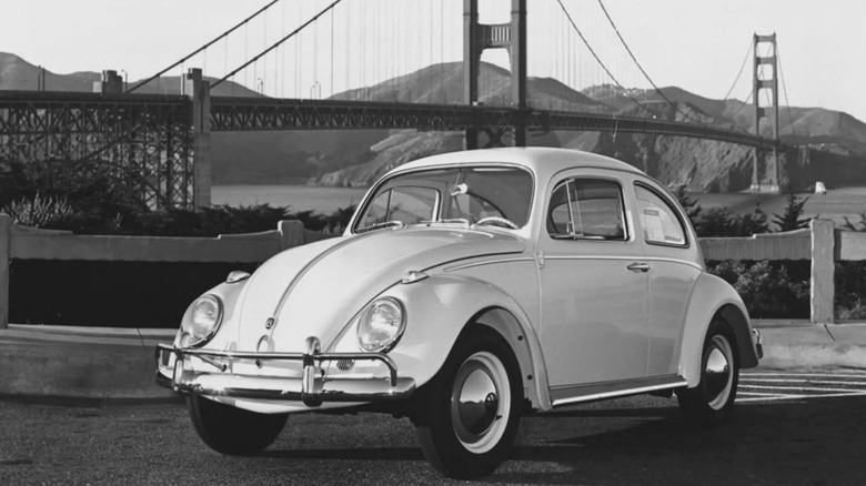 A Black and white picture of a Volkswagen Beetle parked by the Golden Gate Bridge.