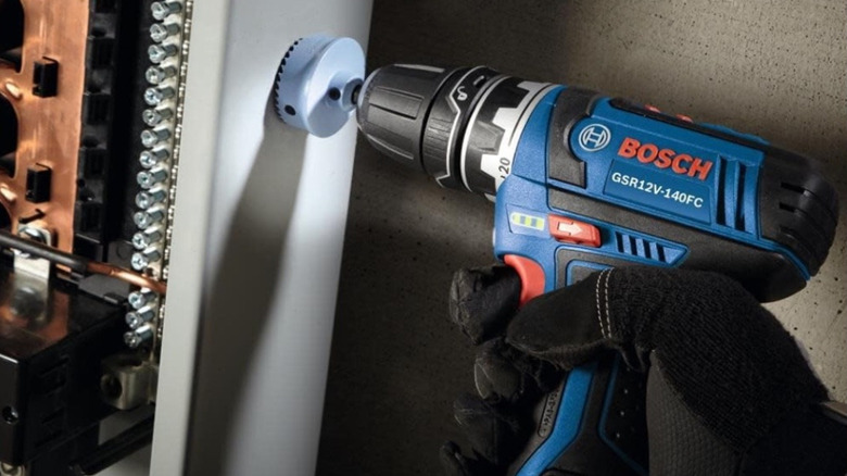 Hand holding Bosch power drill and driver.