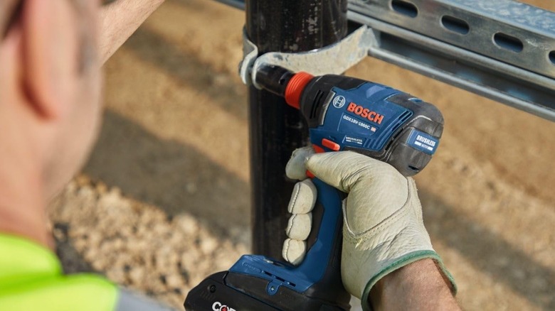 Close-up of hand holding Bosch 18-volt impact driver and wrench tool.
