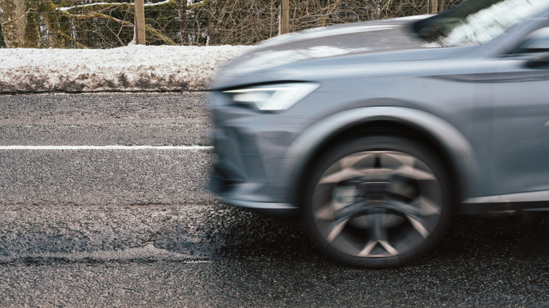 A photo of a blurred blue vehicle driving on wet pavement with a snowy background