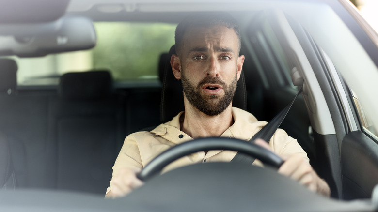 A worried-looking man behind the wheel of a car