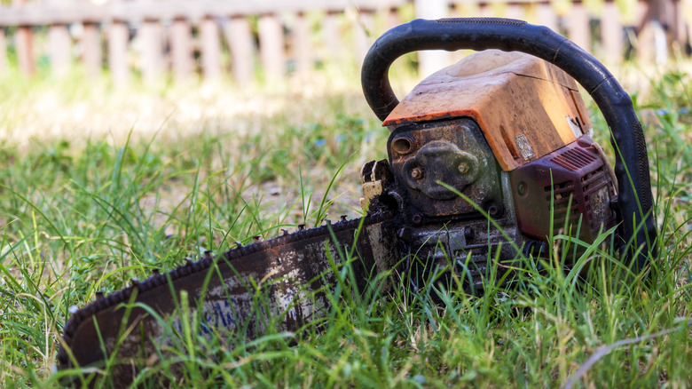An older, dirty chainsaw in the grass.