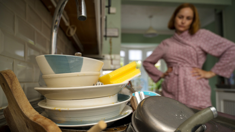 A frustrated woman in a pink bathrobe staring at a stack of dirty dishes