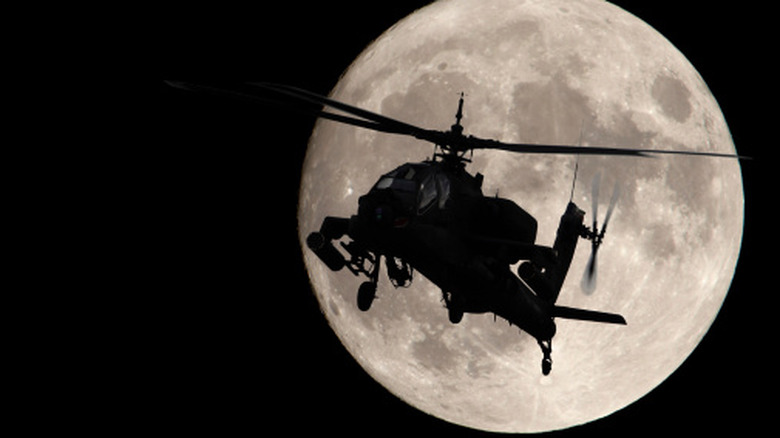 Apache helicopter flying at night with moon in background