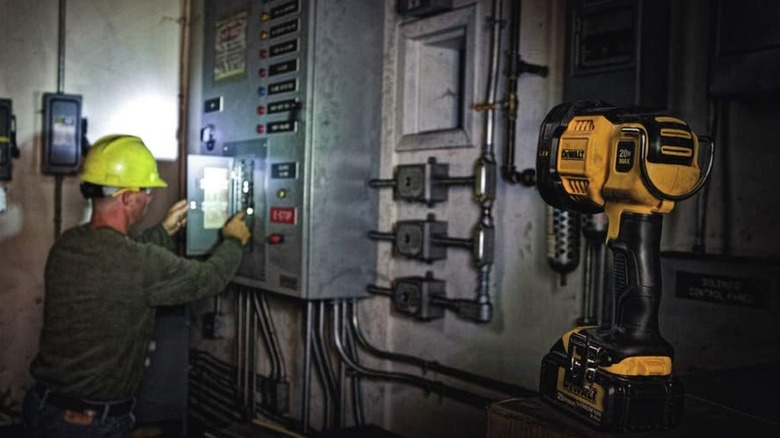 A worker works on an electrical box while illuminated by a DeWalt work light.