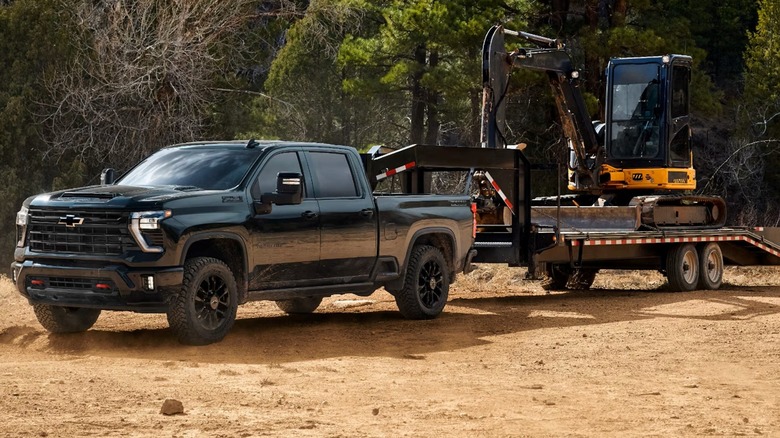 A Chevrolet HD pickup truck hauling heavy equipment on a trailer.
