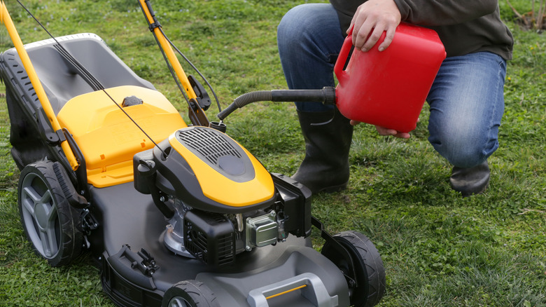 Person pouring fuel into lawn mower.