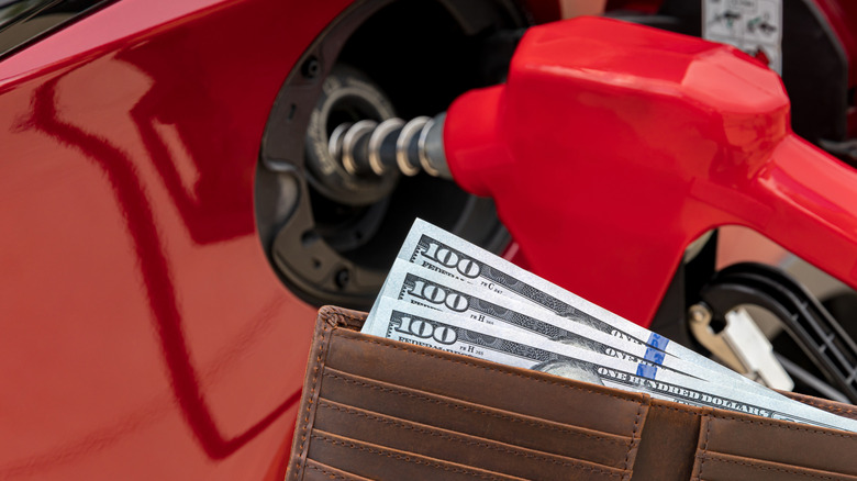 Expensive fuel illustration with a wallet and hundred dollar bills in the foreground with fuel pump handle in the background