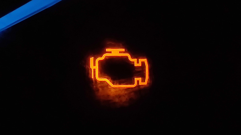 A closeup of a check engine light lit up on the driver instrument panel indicating problems