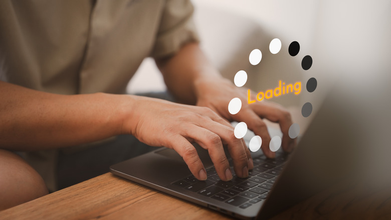 Close up of a person using a laptop with a "loading" icon floating over the keyboard