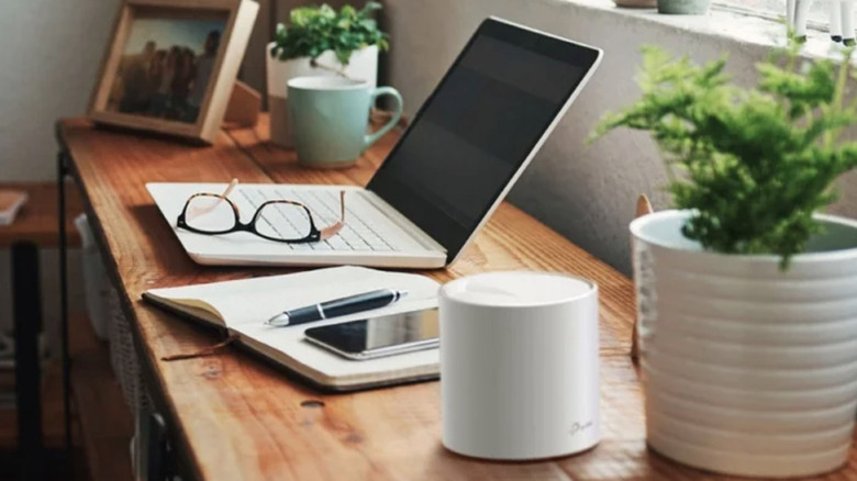 A TP-Link Mesh System router sitting on a wood desk next to a potted plant, an open notebook and other office items