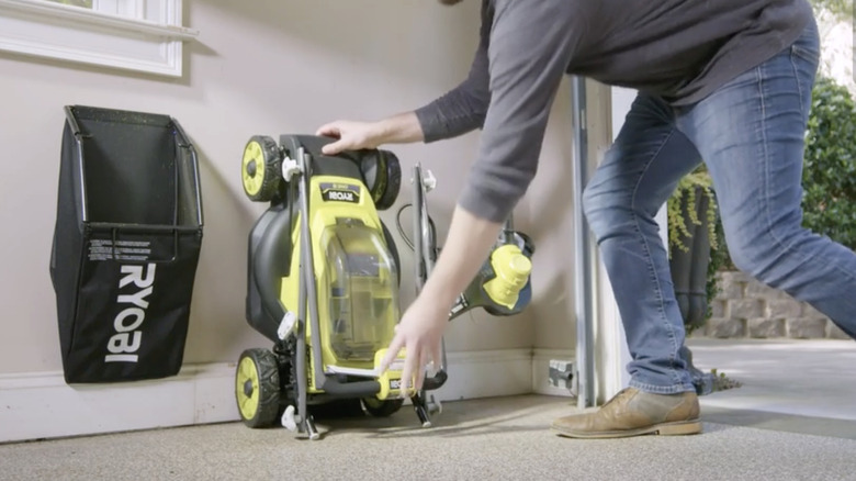 A man folding the Ryobi 18V One+ 13" Mower and storing it in a garage