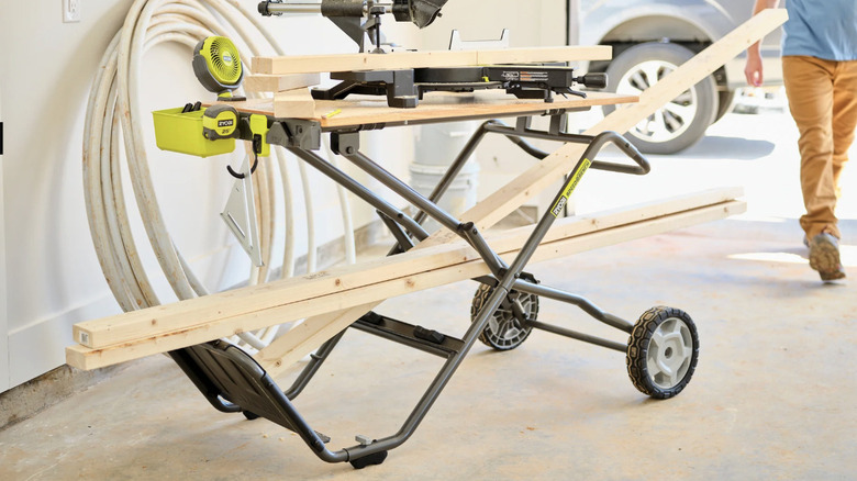 The Ryobi Speed Bench Mobile Workstation set up as a work bench in a garage with a man in the background walking toward it
