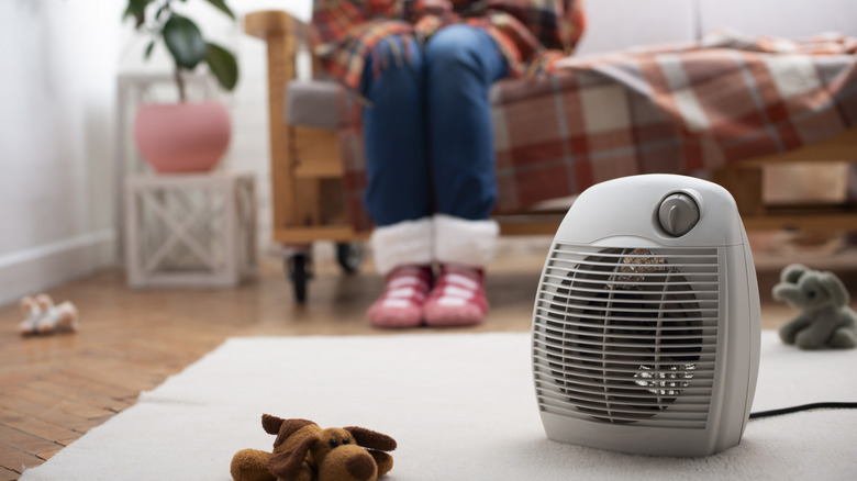 A portable heater on the floor and a lady sitting on the side