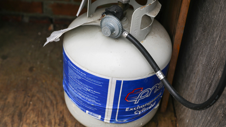 An image of a white propane tank in a wooden storage shed.