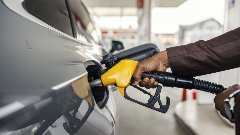 A man's hand holding a fuel pump nozzle, filling up the tank at a gas station.