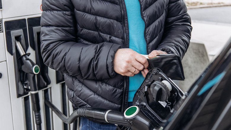Close up of a man holding a wallet while refueling a car at a gas station