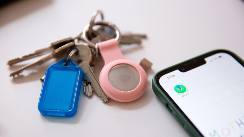An AirTag attached to a bunch of keys placed next to an iPhone scanning for nearby devices