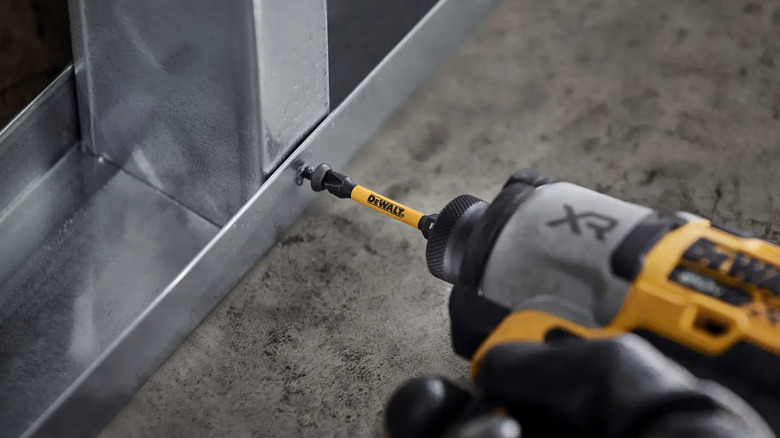 Person using yellow impact driver with DeWalt bit to drive screw into metal framing