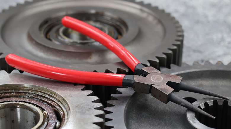 A set of snap ring pliers laid across three large gears.