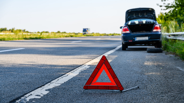 Car on side of road with orange caution sign