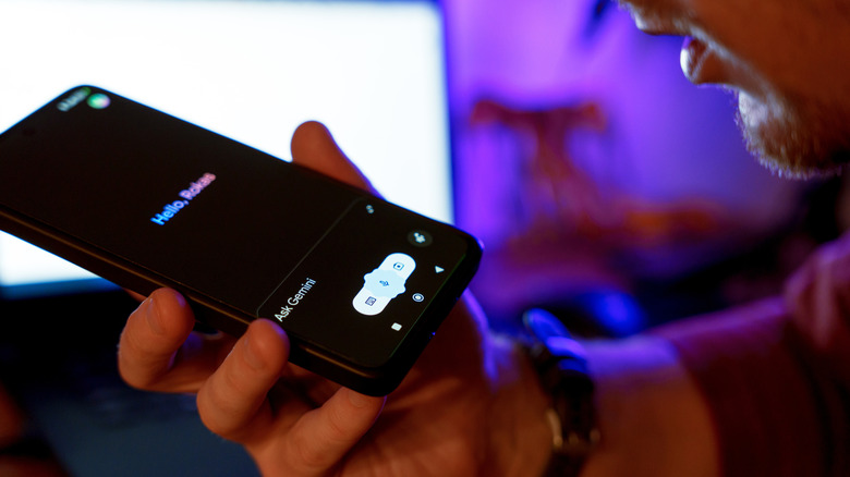 A man speaks to Google Assistant on his phone, TV in background