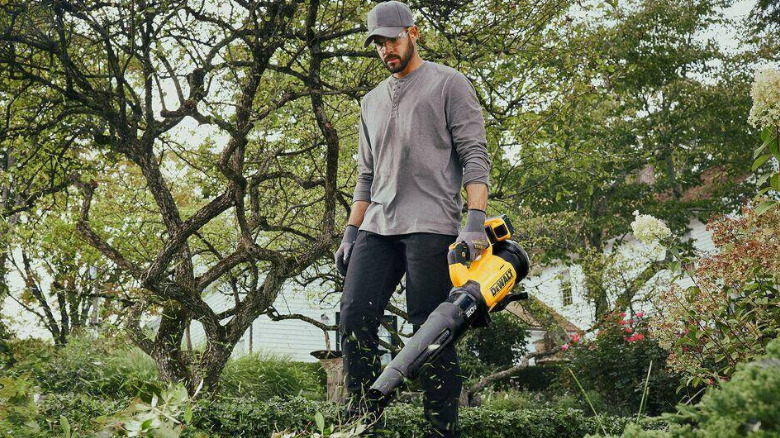 A person using a 20V Max XR Brushless Cordless Blower to move leaves in a garden.
