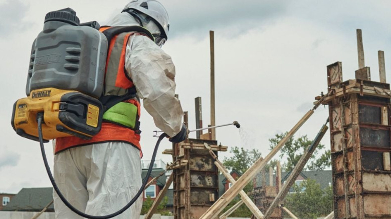A person wearing a protective suit and carrying the 20V Max XR Concrete Chemical Sprayer.