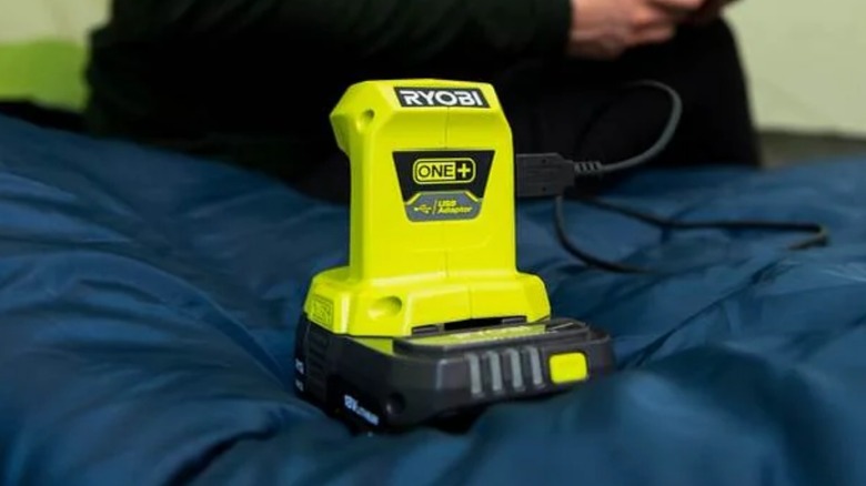 A person using a Ryobi charging adapter in a tent.